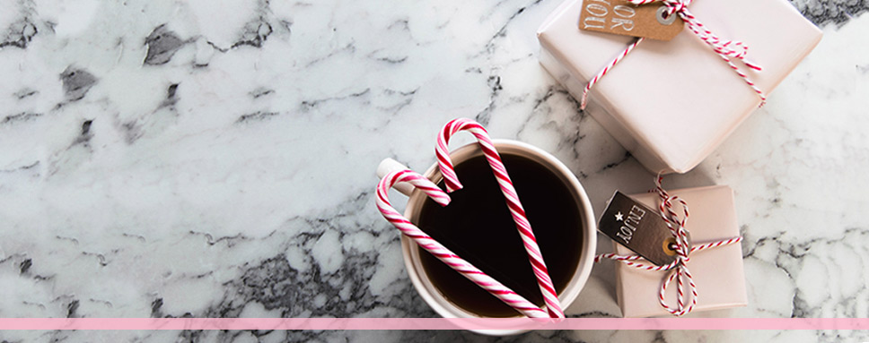 Kaffekopp, polkagris och rosa paket mot vit marmorbakgrund, god jul önskar Amendo
