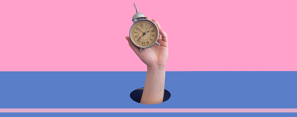 Hand håller analog klocka mot blå och rosa bakgrund, Amendo